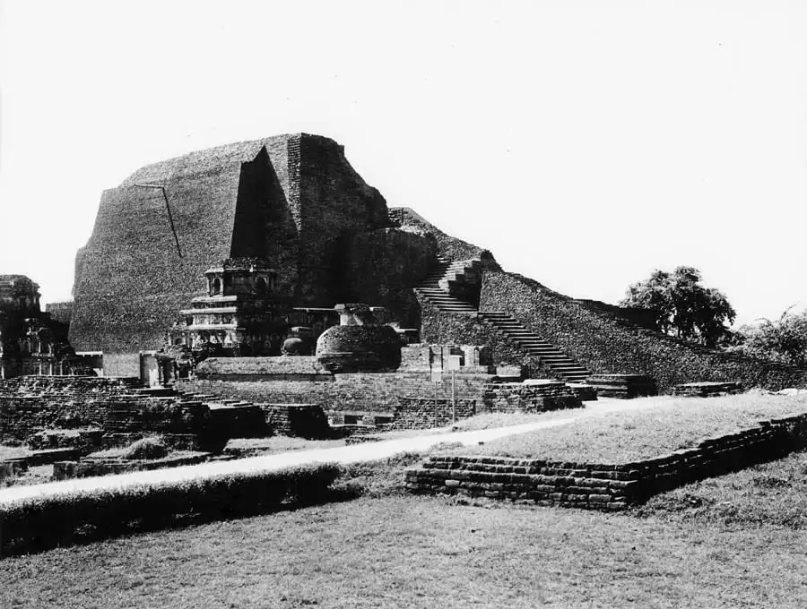 The ruins of Stupa 3 at Nalanda: a high brick mound with a stepped
stairway up its face, votive shrines along its base, and the excavated
foundations of the monastery running away across cut grass